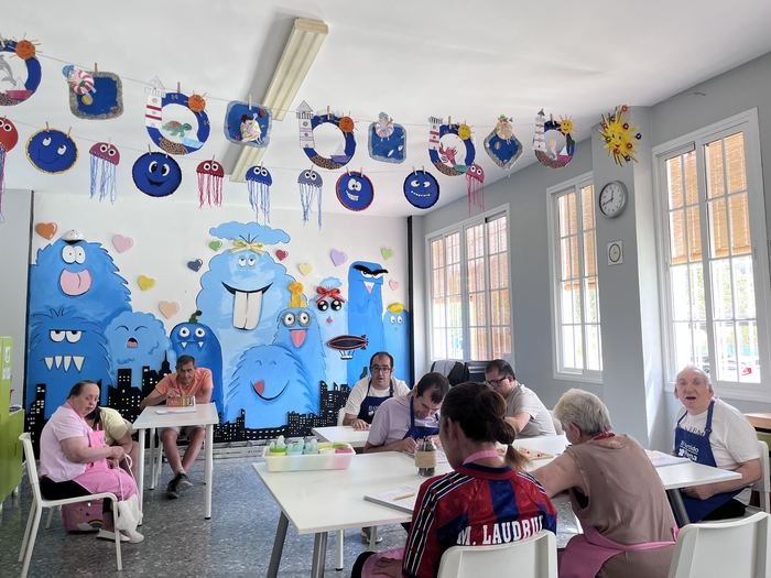 Sala de taller con mural infantil de colores en la pared y personas trabajando en las mesas