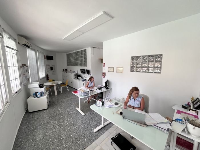 Despacho de dirección con mesas de trabajo, ventanales y dos profesionales trabajando