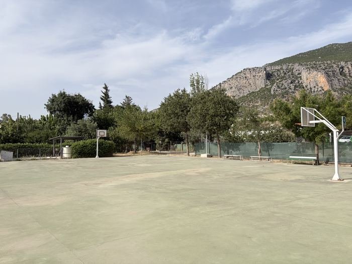 Pista polideportiva del patio con canasta de baloncesto y montañas al fondo