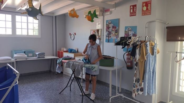 Lavandería del centro con zona de planchado y ropa colgada, con una profesional planchando